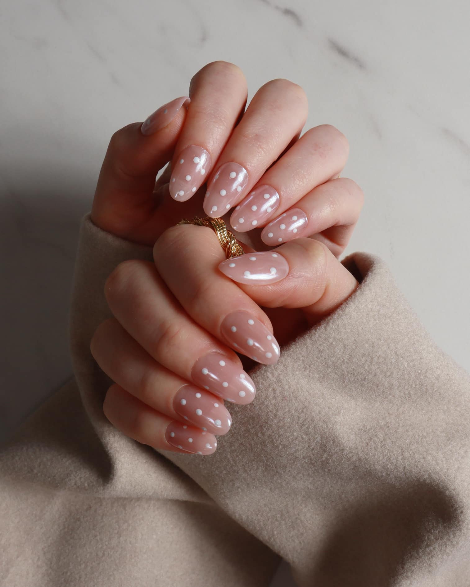 Close-up of hands with pink polish with polka dot art on a neutral background