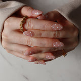Close-up of hands with polka dot nail design and gold rings on a neutral background