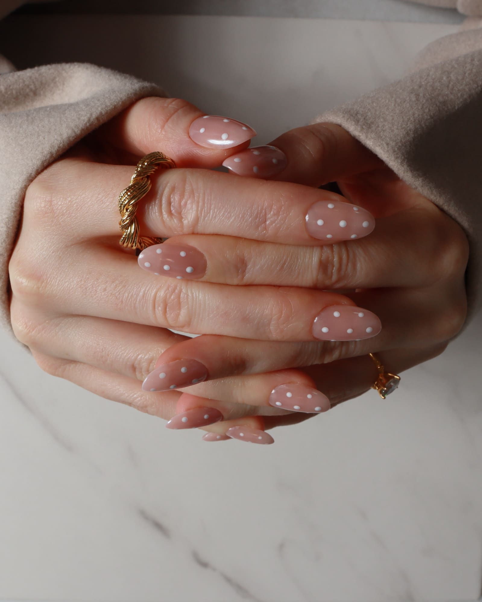 Close-up of hands with polka dot nail design and gold rings on a neutral background
