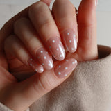 Hand with pink nail polish featuring white polka dots on a neutral background
