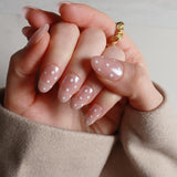 Hand with polka dot nail design wearing a gold ring on a neutral background