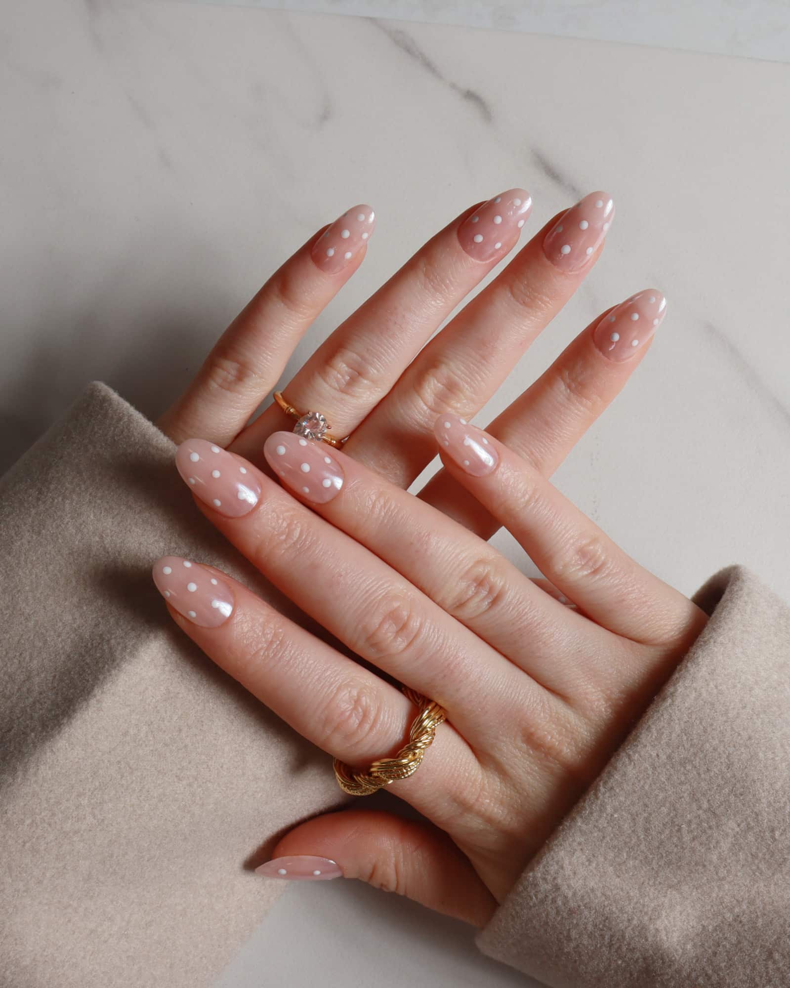 Hand with pink nail polish and gold rings on a neutral background