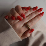Hand with red nail polish and a gold ring on a neutral background