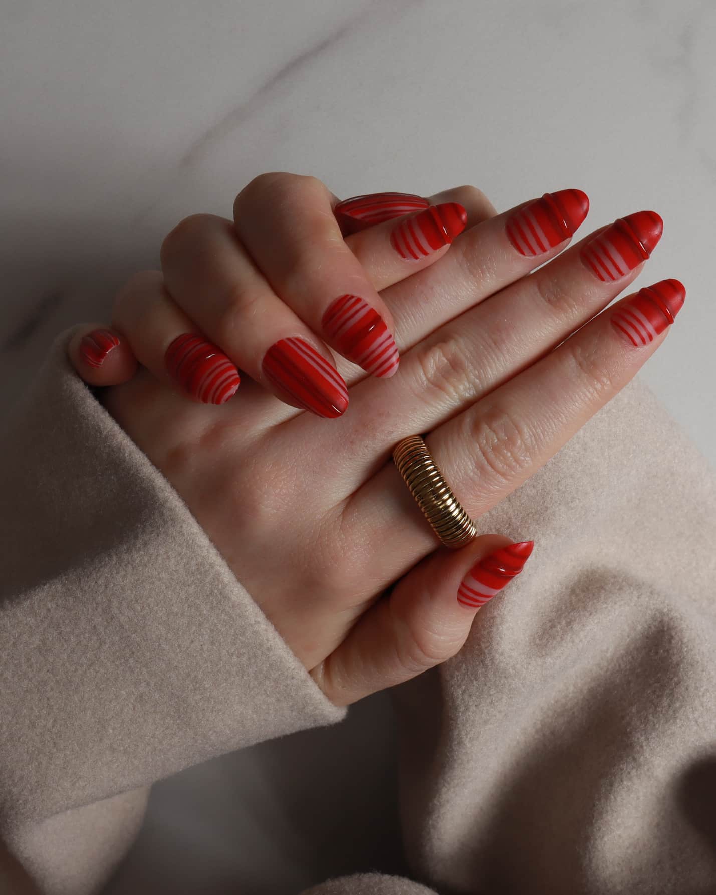 Hand with red nail polish and a gold ring on a neutral background