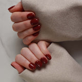 Close-up of hands with dark red nail polish wearing a beige coat.
