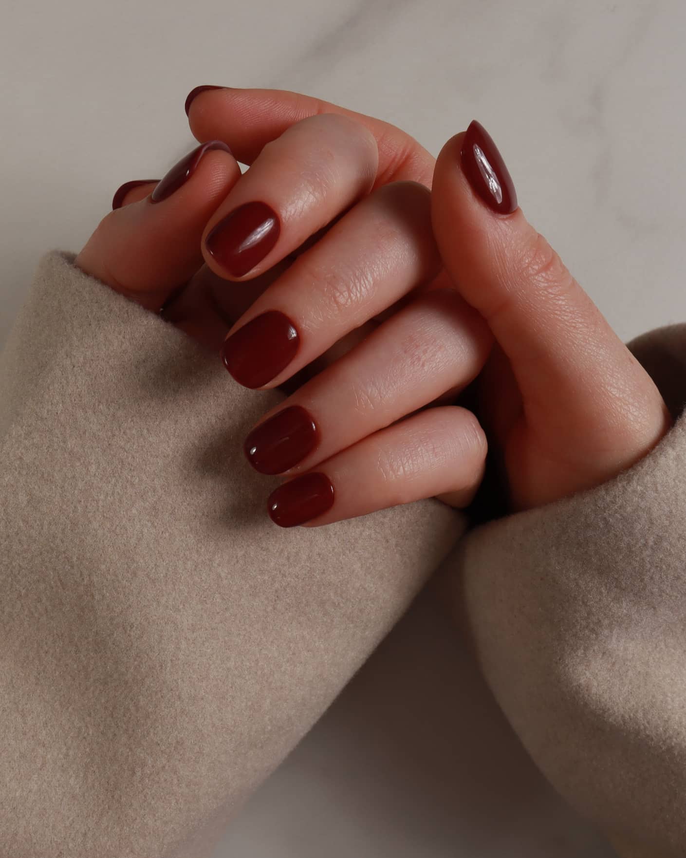 Close-up of hands with dark red nail polish wearing beige gloves.