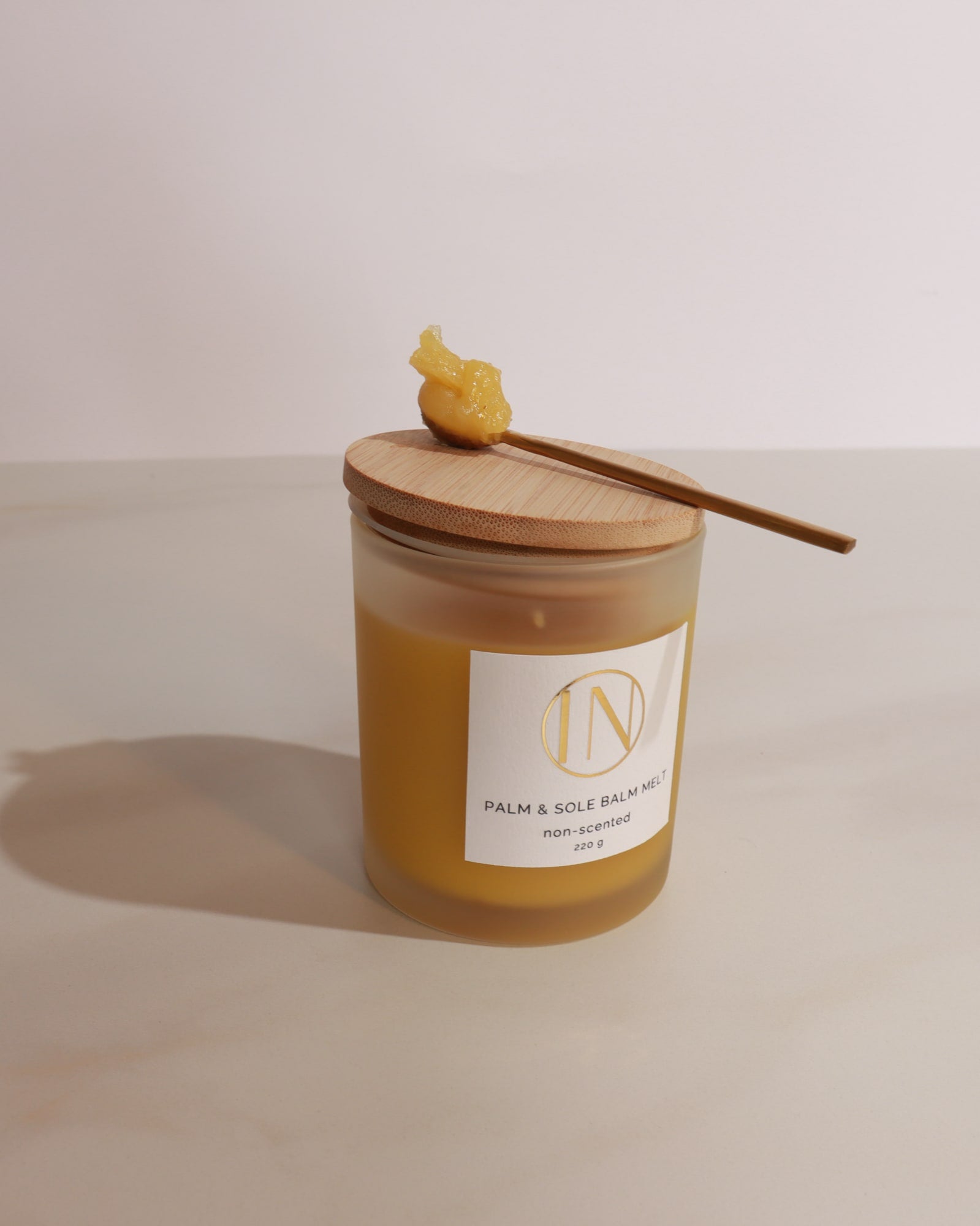 Jar of palm and sole balm with wooden applicator on a light background