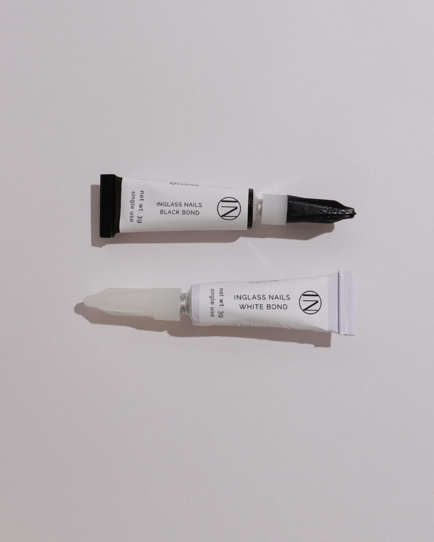 Two tubes of nail bond product on a light gray background