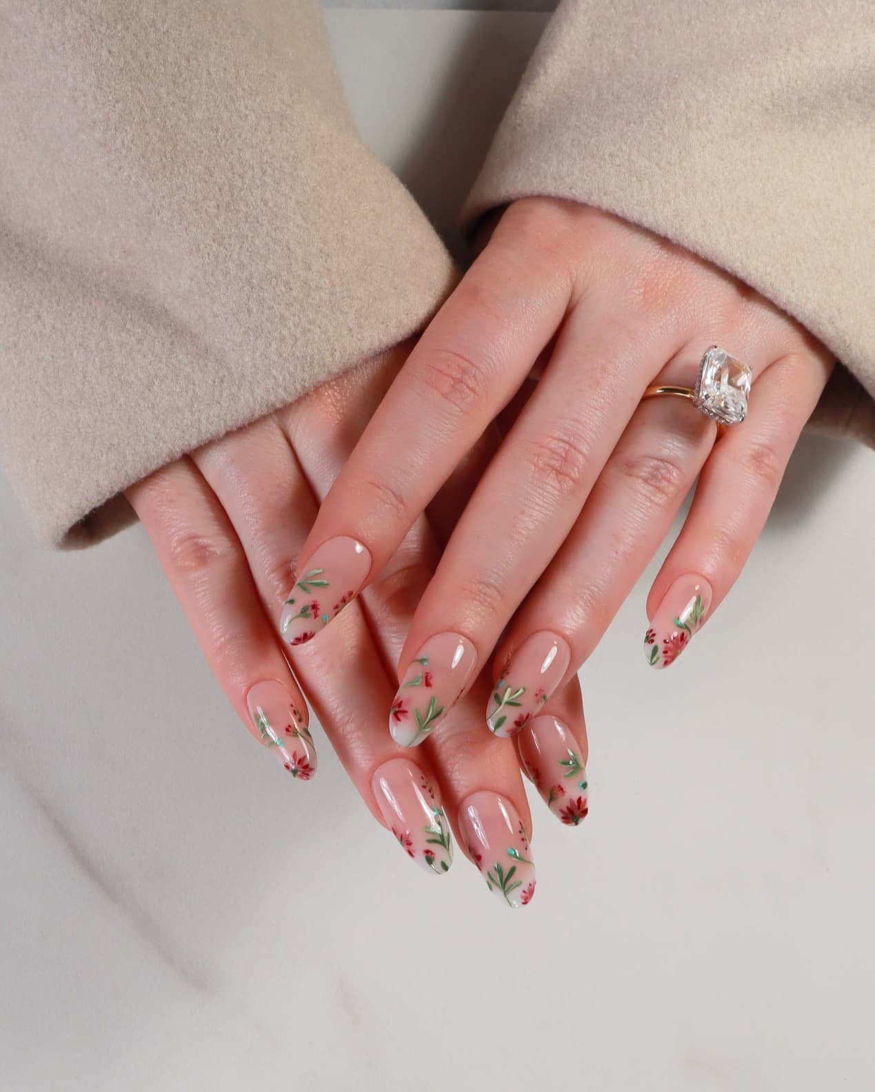 Close-up of hands with floral nail design wearing a beige coat.