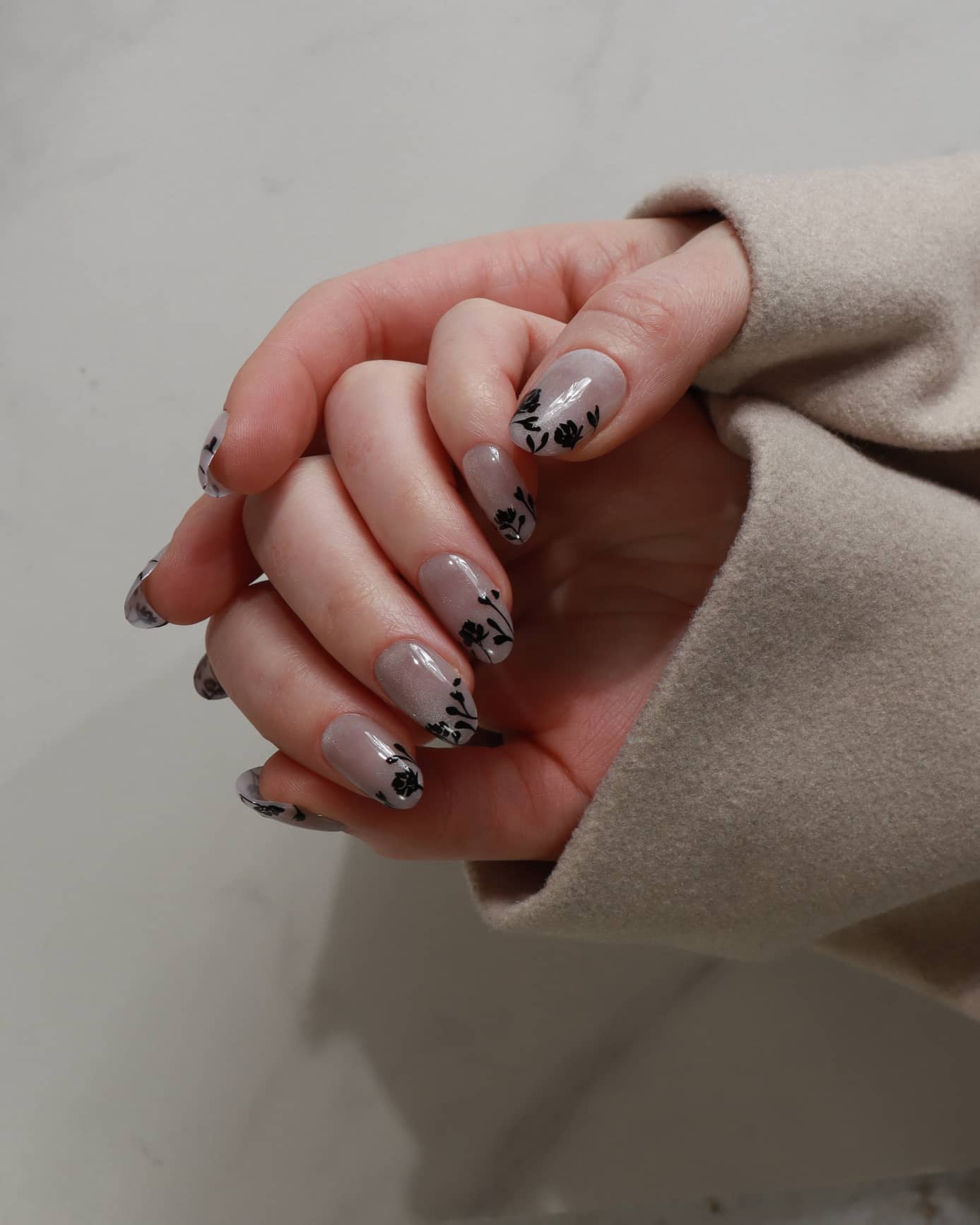 Close-up of hands with floral nail design on a neutral background
