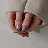 Close-up of a hand with gray nail polish and black floral designs on a neutral background