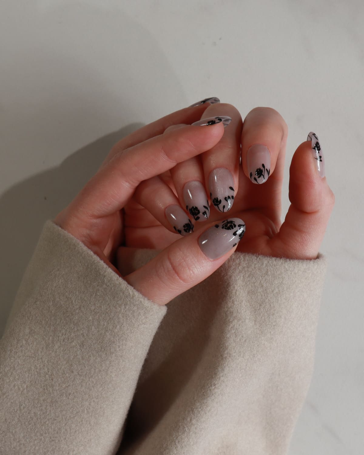 Hand with gray nail polish and black floral designs on a neutral background