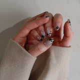 Hand with gray nail polish and black floral designs on a neutral background